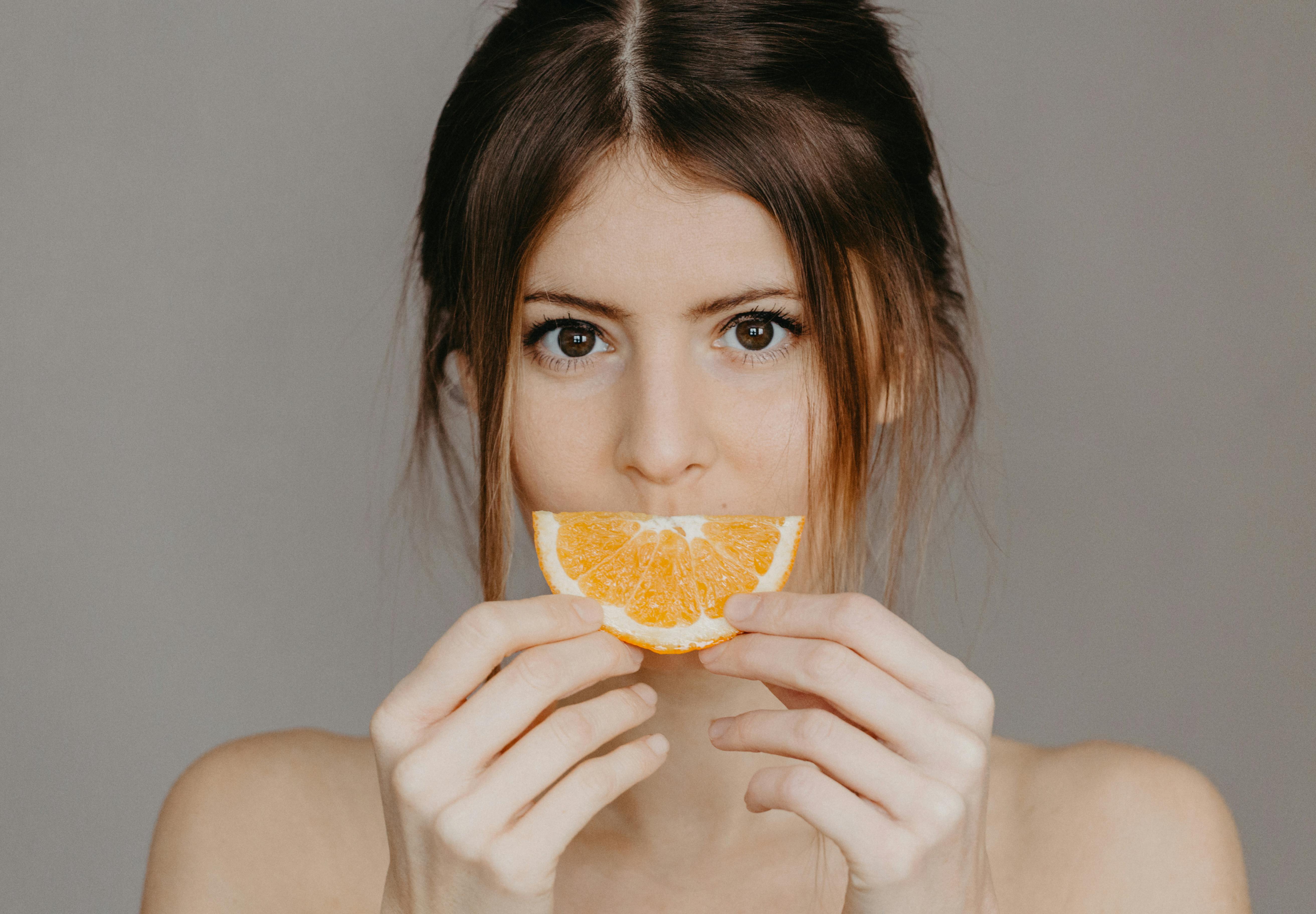Close-up portrait of a woman holding a half orange slice, with a focus on natural beauty and skincare.